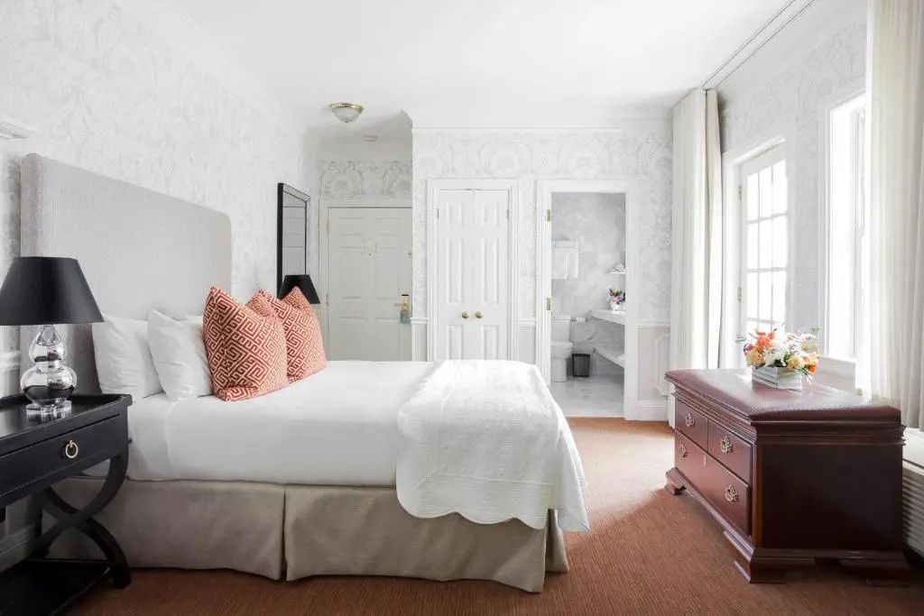 Schlafzimmer mit Doppelbett, orangen Kissen und offener Badezimmertür