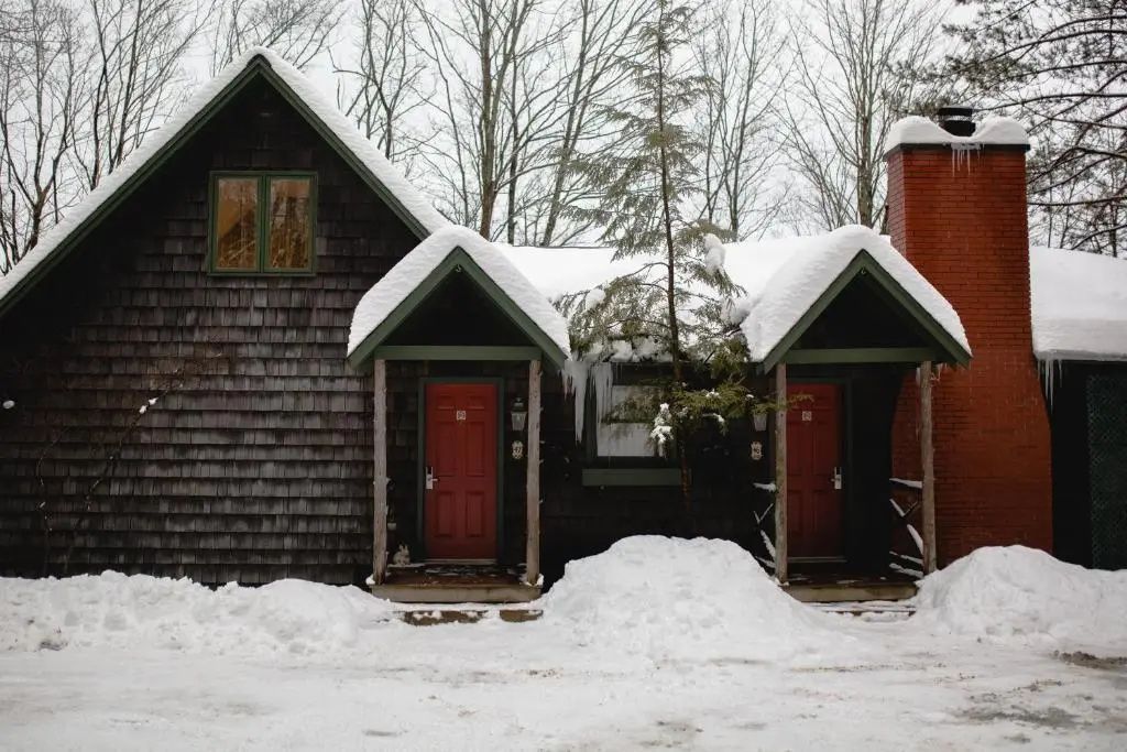 Schneebedeckte Hütte mit zwei roten Türen vor winterlicher Kulisse