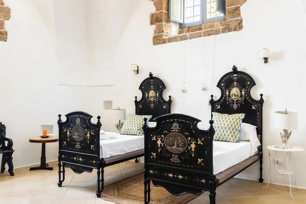 Zwei antike Metallbetten in stilisiertem Zimmer mit historischen Steinfenstern.