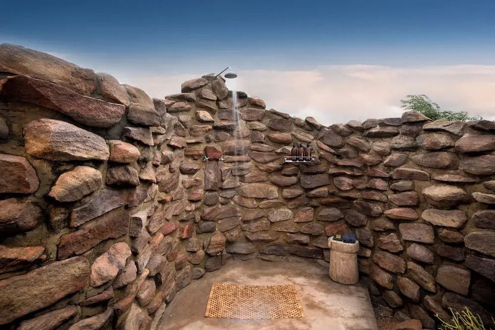 Offene Dusche aus Natursteinen unter freiem Himmel für ein authentisches Safari-Erlebnis