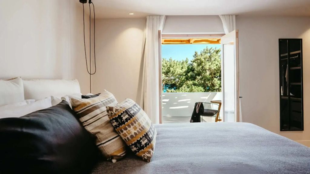 Helles Schlafzimmer mit offenen Vorhängen und Blick auf Balkon und Bäume