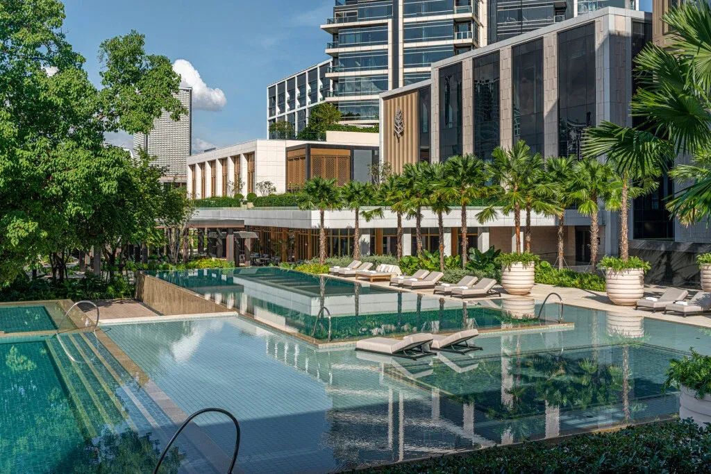 Luxuriöser Hotelpool mit Liegen umgeben von Grünflächen und moderner Architektur.