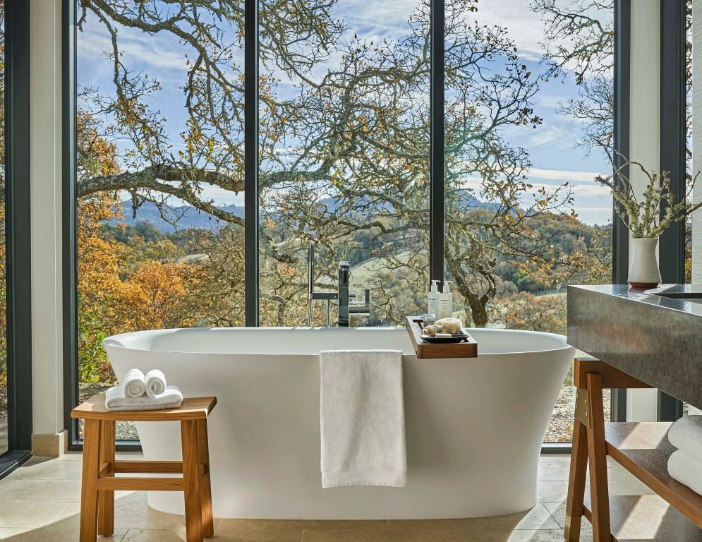 Freistehende Badewanne mit Aussicht auf herbstliche Landschaft durch große Fenster