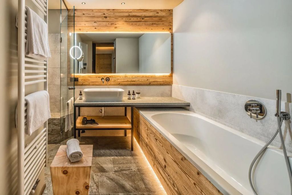 Luxuriöses Badezimmer mit Badewanne und beleuchtetem Spiegel in Holzoptik.