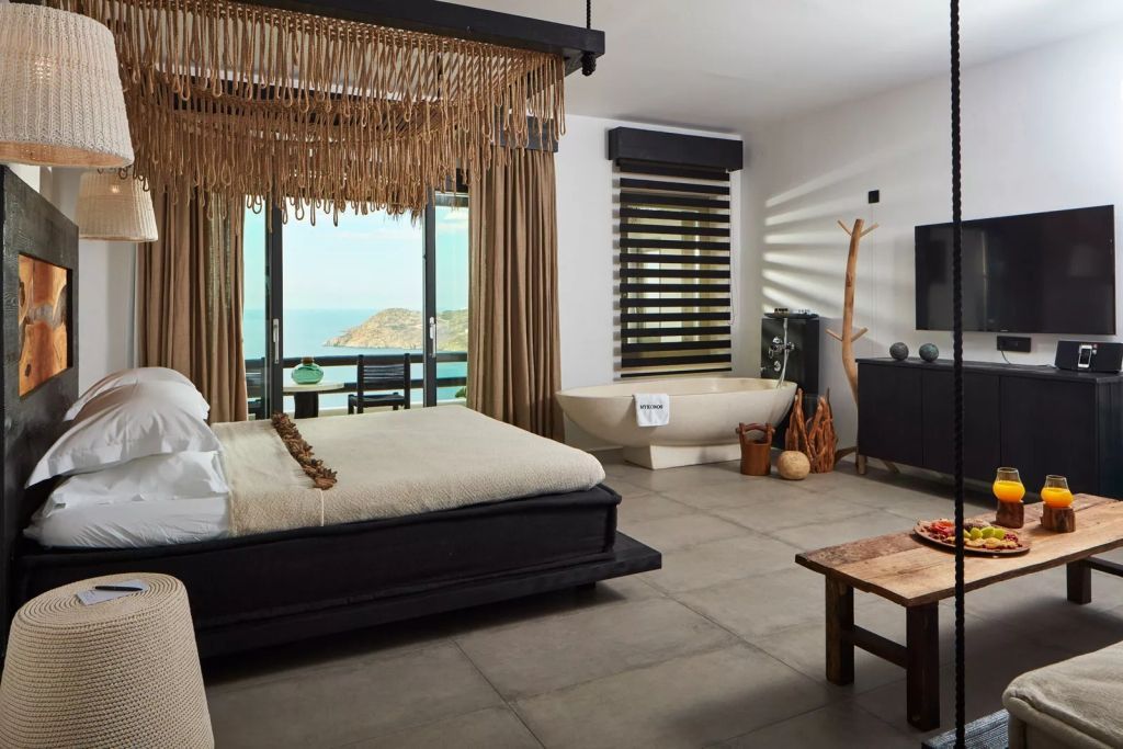 Geräumige Hotelsuite mit modernem Interieur, Doppelbett, freistehender Badewanne und Meerblick.