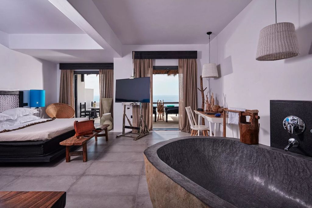 Elegante Suite mit großem Bett, Badewanne und Meerblick von der Terrasse.