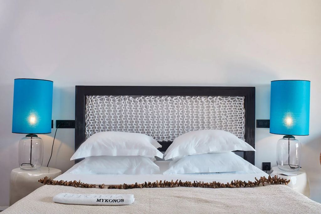 Modernes Doppelbett mit kunstvoll gestaltetem Kopfteil und weißen Kissen im Myconian Utopia