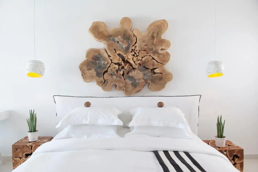 Doppelbett mit weißer Bettwäsche vor einer dekorativen Wandkunst aus Holz.