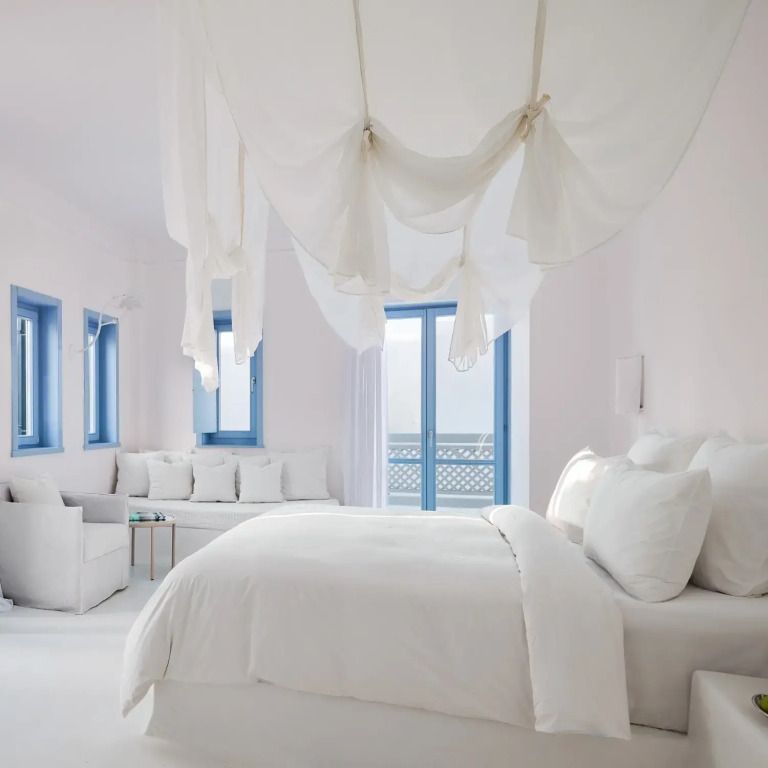 Helles Zimmer mit weißem Doppelbett und blauen Fensterrahmen