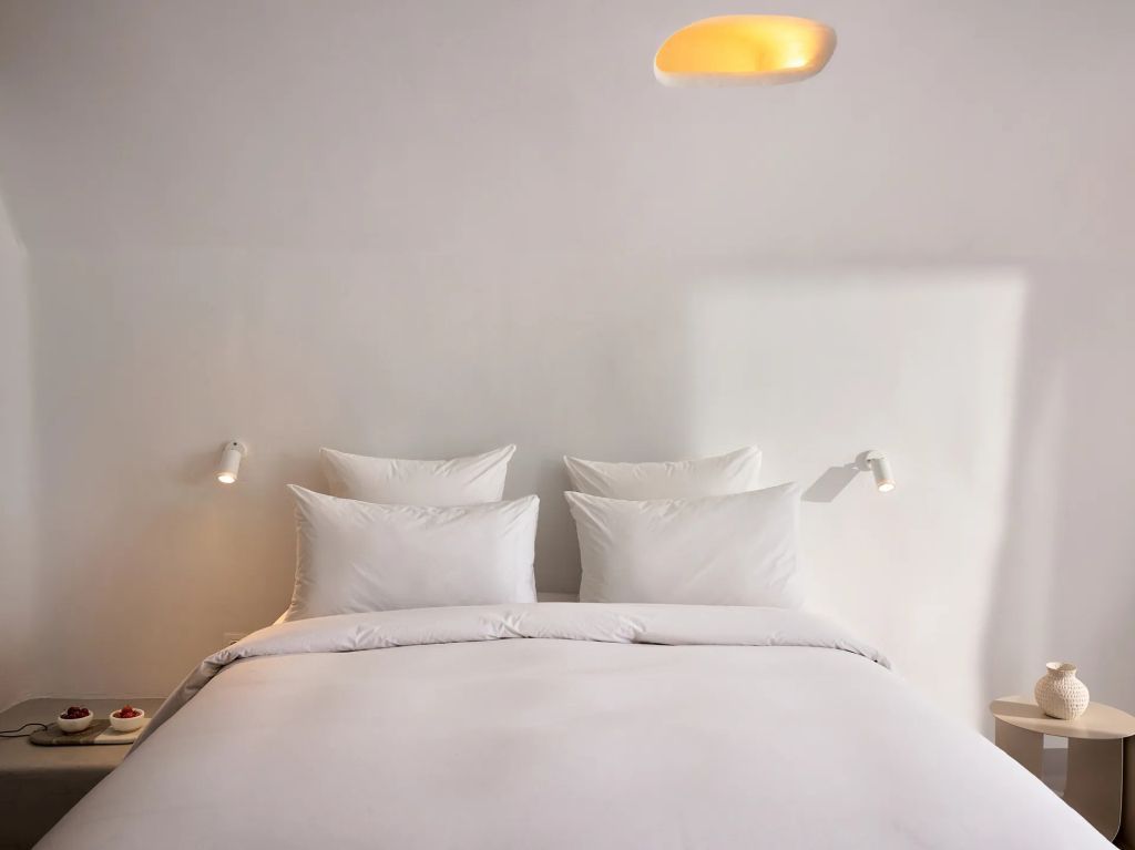 Modernes Doppelbett mit weißen Kissen und schlichter, eleganter Beleuchtung.