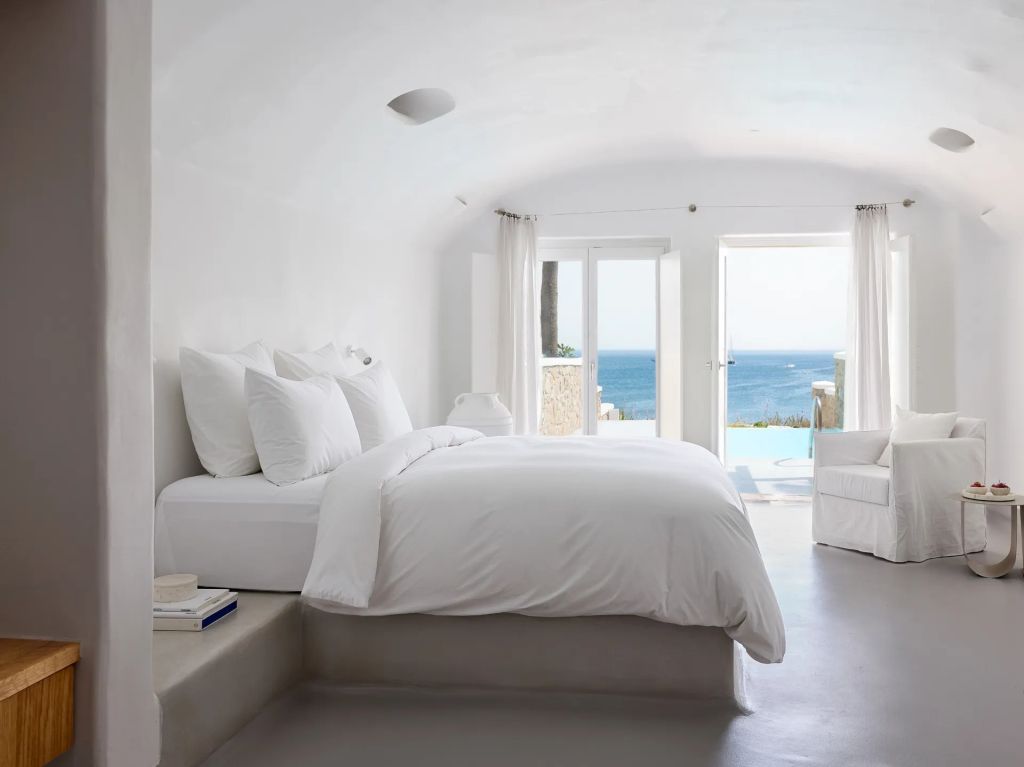 Helles Schlafzimmer mit Doppelbett und Meerblick durch offene Terrassentüren.