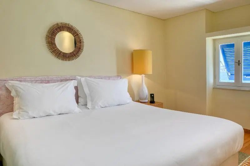 Helles Doppelzimmer mit großem Bett, Lampe und rundem Spiegel