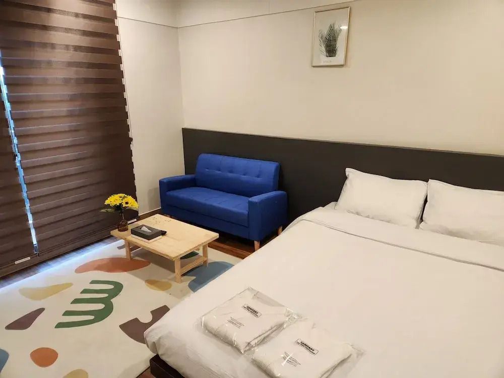Modernes Hotelzimmer mit Doppelbett, blauer Couch und dezenter Dekoration.