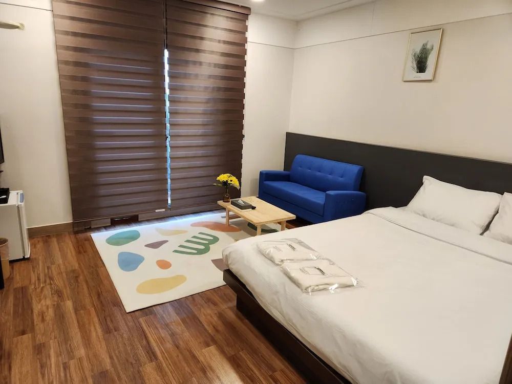 Geräumiges Hotelzimmer mit Doppelbett, bunter Teppich und blauer Couch.