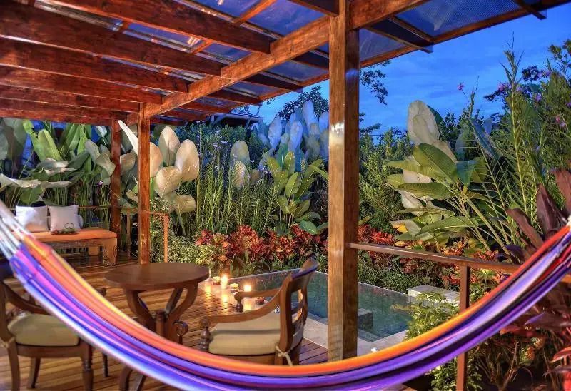 Terrasse mit Holzdach und luxuriösen Möbeln mit Blick auf dichte Vegetation und Pool