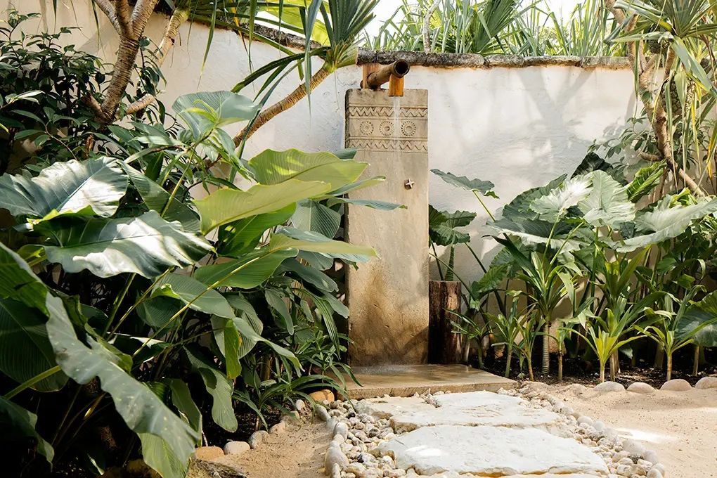 Dusche im Freien umgeben von üppigem Grün und Natursteinen.