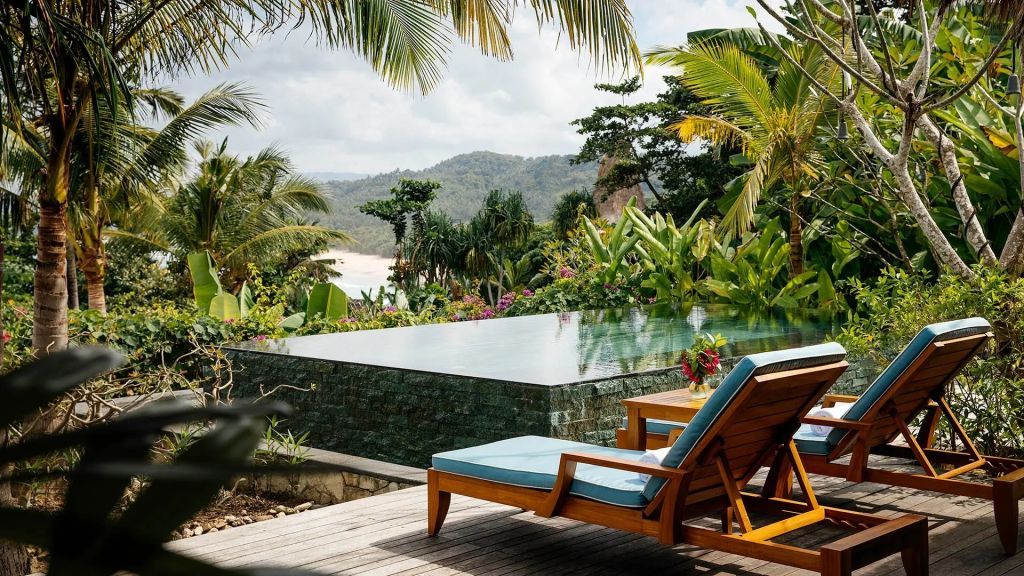 Infinity-Pool mit Liegestühlen umgeben von tropischen Pflanzen und Palmen