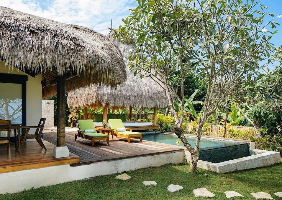 Private Villa-Terrasse mit Strohdach, Pool und Sonnenliegen im Grünen.