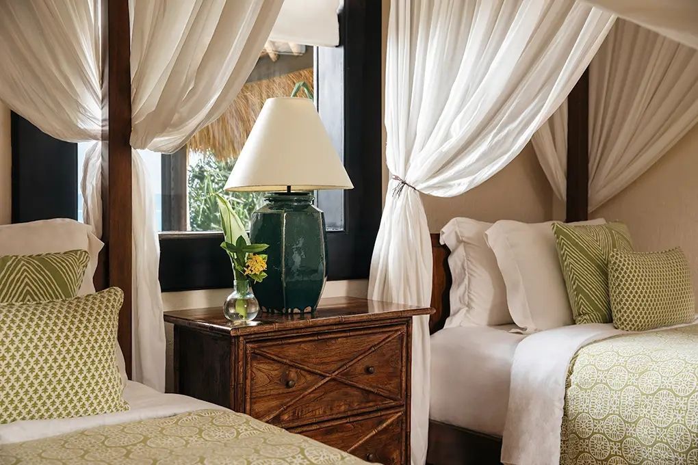 Elegantes Schlafzimmer mit Himmelbetten, hölzernem Nachttisch und grüner Tischlampe.