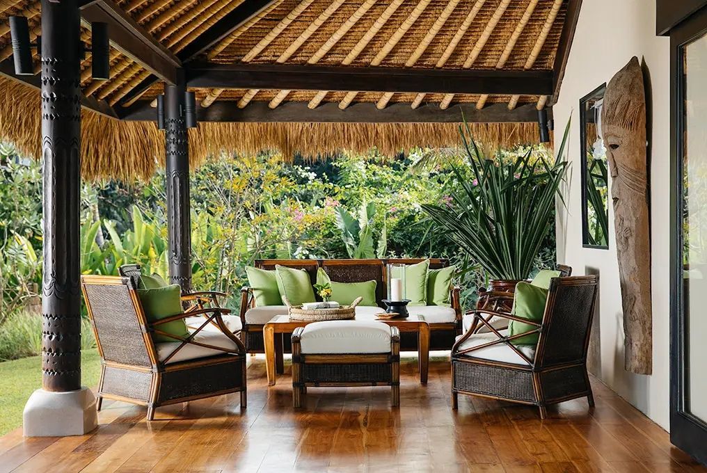 Lounge-Bereich in der Villa mit Rattanstühlen und üppigem Gartenblick.