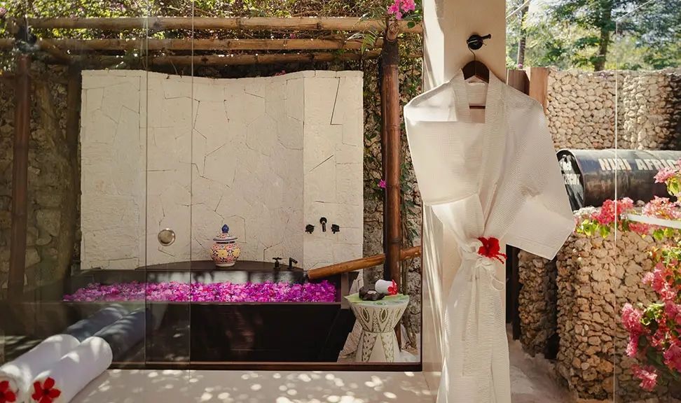 Luxuriöses Badezimmer mit steinerner Badewanne und Rosenblüten, edler Kimono am Haken