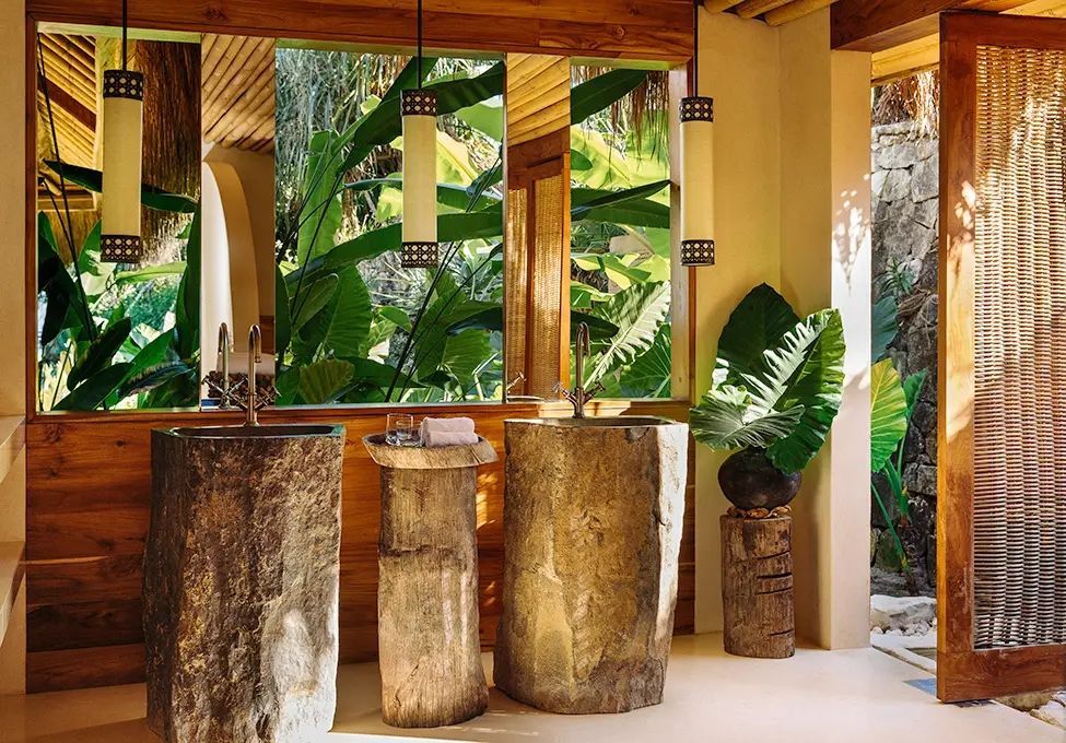 Stylisches Badezimmer mit Natursteinwaschbecken und großem Spiegel in tropischer Umgebung