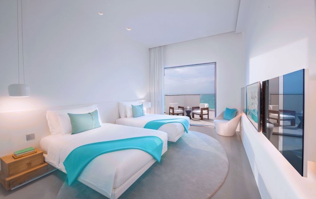Modernes Zimmer mit zwei Einzelbetten, türkisfarbenen Akzenten und Zugang zum Balkon mit Meerblick
