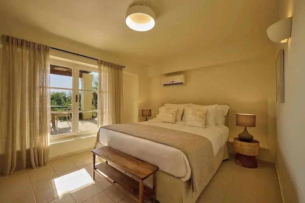 Helles Schlafzimmer mit einem großen Bett und Zugang zu einer Terrasse mit Gartenblick.