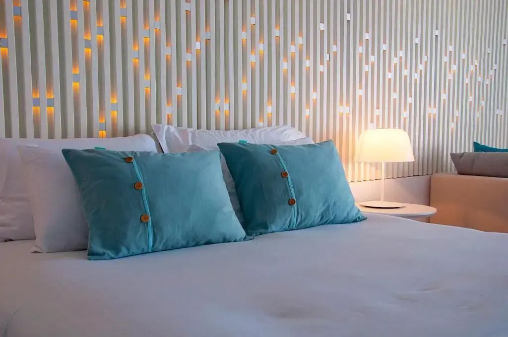 Doppelbett in der Suite mit blau-grünen Kissen und stilvoller Beleuchtung.