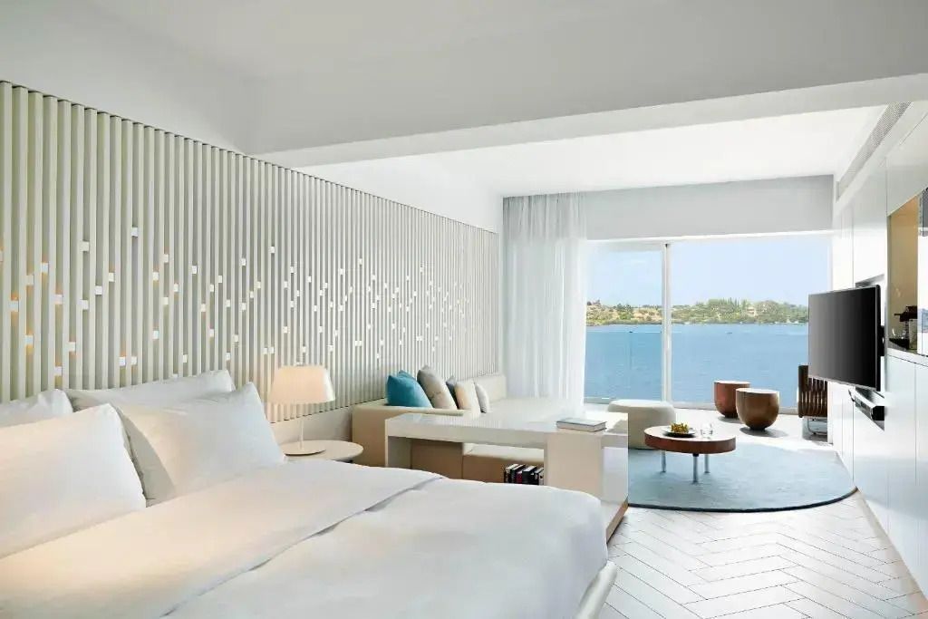 Helles Hotelzimmer mit Doppelbett und Meerblick durch große Fensterfront