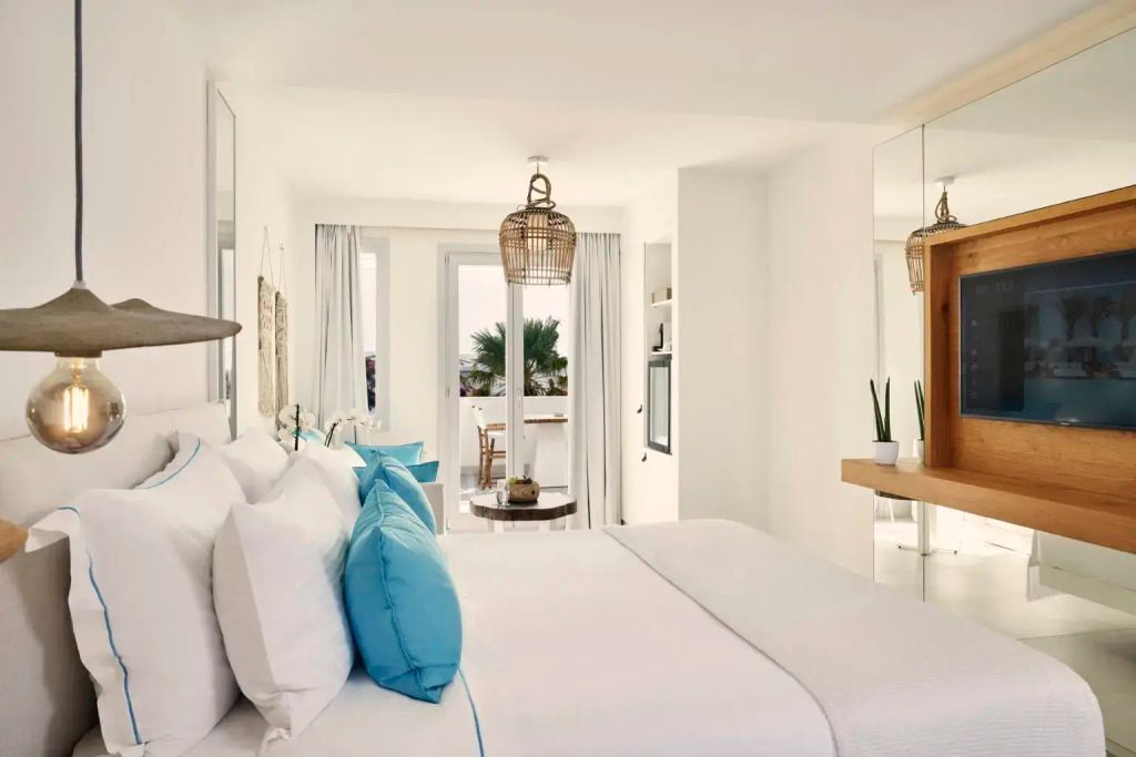 Gemütliches Zimmer mit Doppelbett, Sitzbereich und Balkonblick auf Palmen
