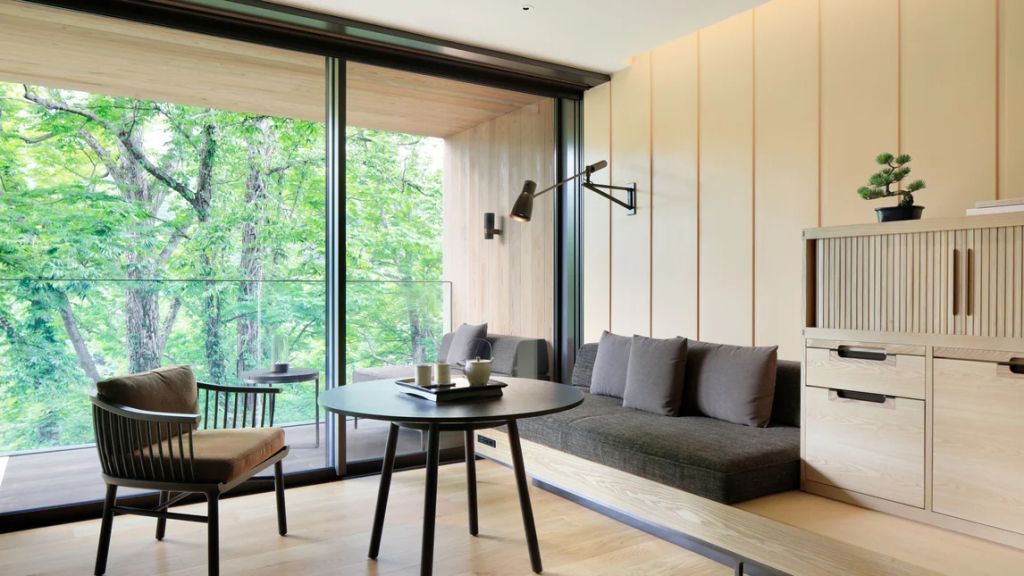 Sitzbereich mit Tisch und Sofas vor einem großen Fenster mit Blick auf die Natur