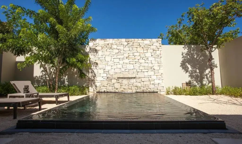 Moderner Pool mit Wasserspiel vor einer Steinmauer und umgeben von Natur