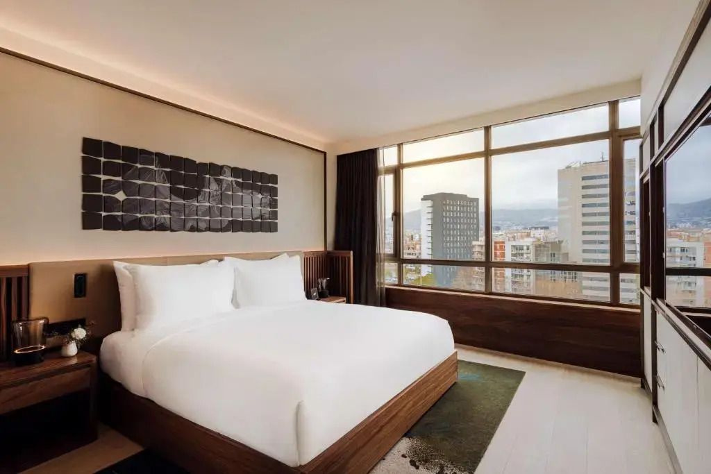 Modernes Hotelzimmer mit großem Fenster und Doppelbett mit weißer Bettwäsche