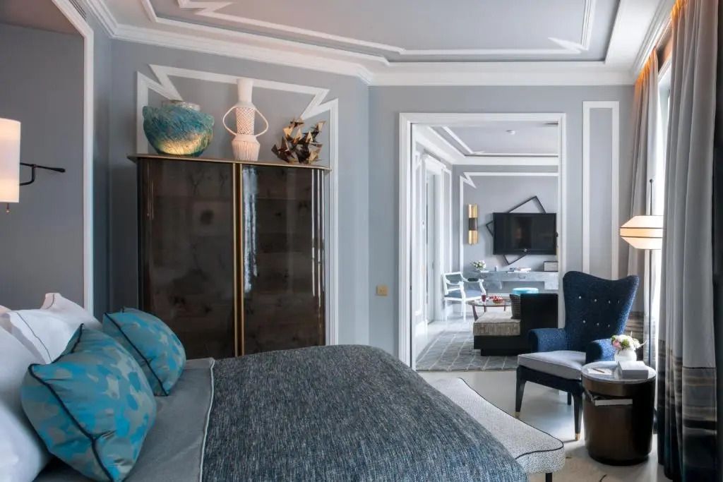 Elegantes Schlafzimmer mit grauer Bettwäsche und Blick auf stilvolles Wohnzimmer.