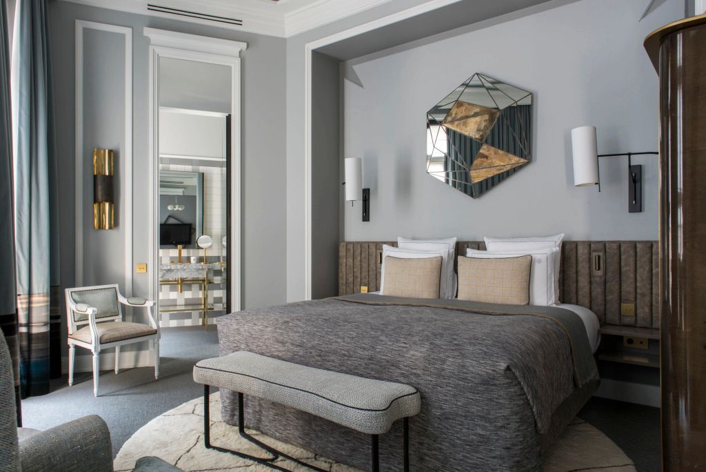Luxuriöses Schlafzimmer mit Spiegel, moderner Kunst und grauer Bettdecke.