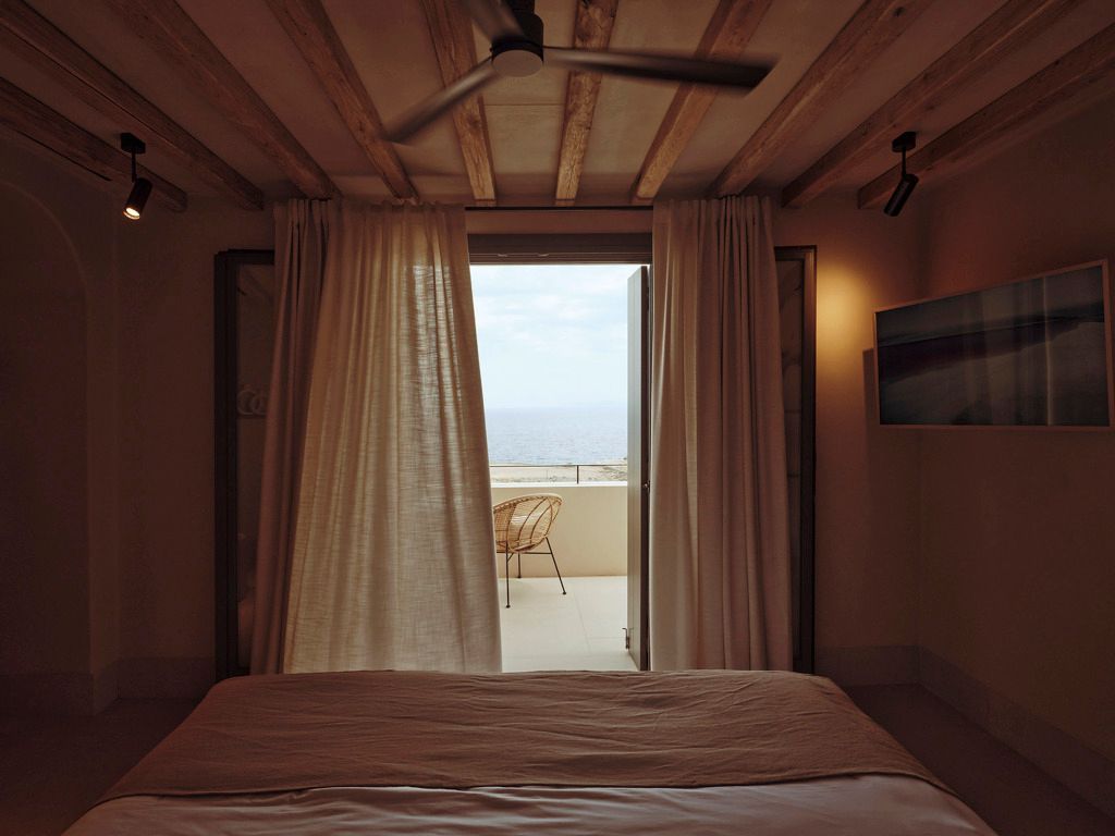 Zimmer mit offenem Vorhang und Aussicht auf eine Terrasse mit Meerblick