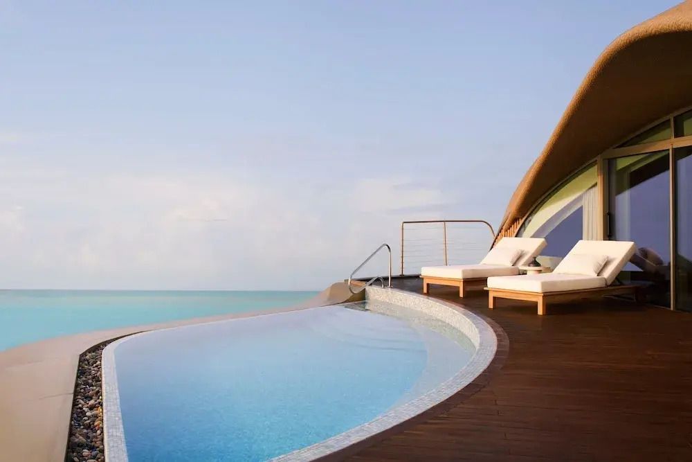 Infinity-Pool mit Meerblick und luxuriösen Sonnenliegen auf einer Holzterrasse.