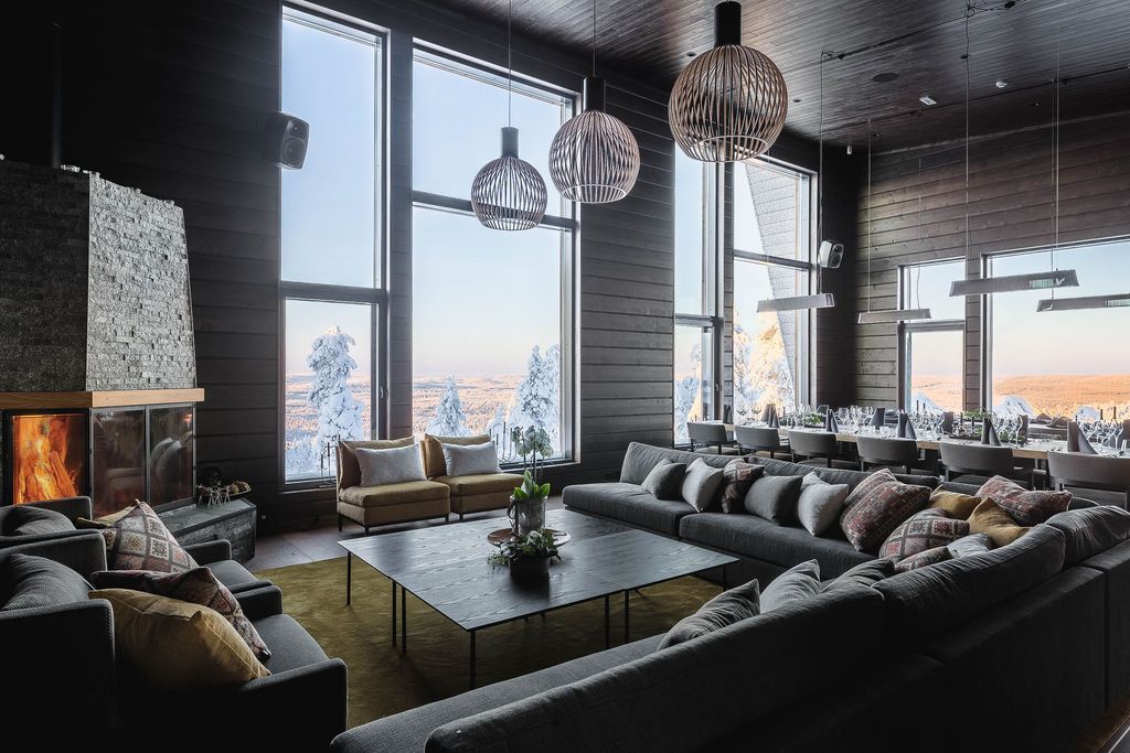 Lounge der Octola Lodge mit Kamin, großen Sofas und raumhohen Fenstern zum verschneiten Wald