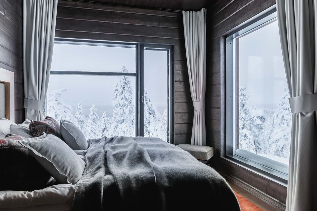 Schlafzimmer der Octola Lodge mit Doppelbett, Vorhängen und Fenstern zum verschneiten Wald