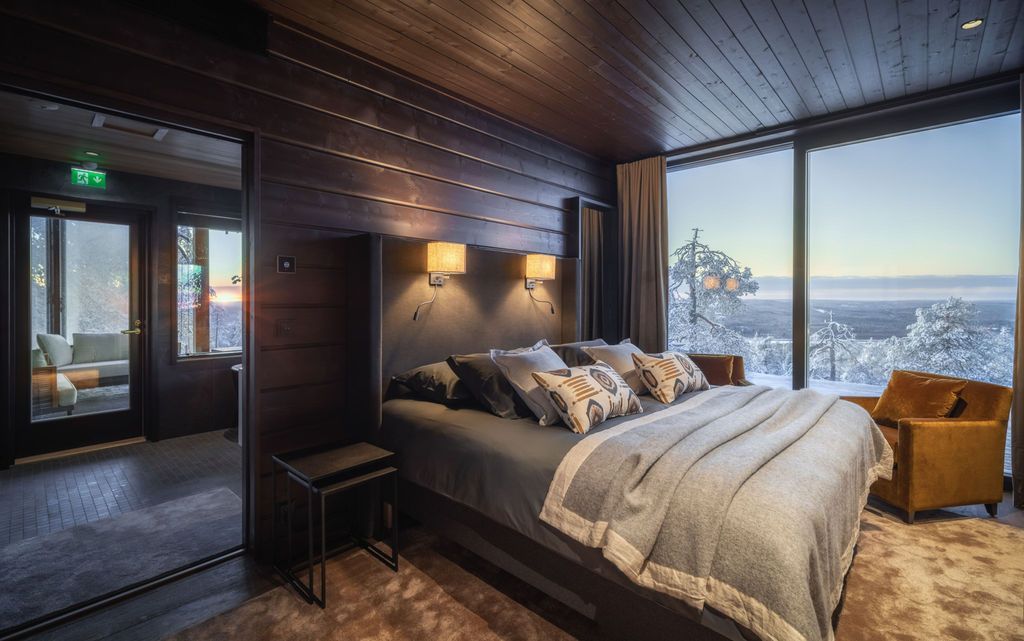 Hauptschlafzimmer der Octola Villa mit Doppelbett, Sessel und Panoramafenster zur Winterlandschaft