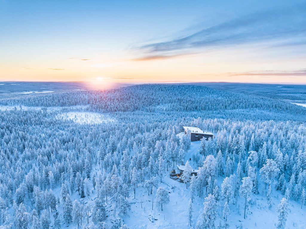Luftbild der verschneiten Wildnis bei Sonnenaufgang mit einem einzelnen Gebäude im Wald