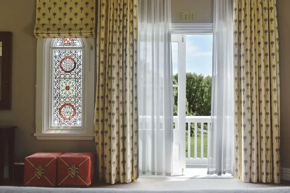 Zimmer mit kunstvoll gestaltetem Glasfenster und Zugang zum Gartenbalkon