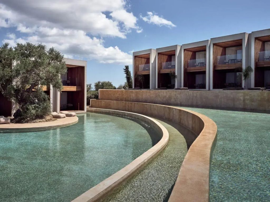Infinity-Pool mit geschwungenen Linien vor einer modernen Hotelkulisse und blauem Himmel