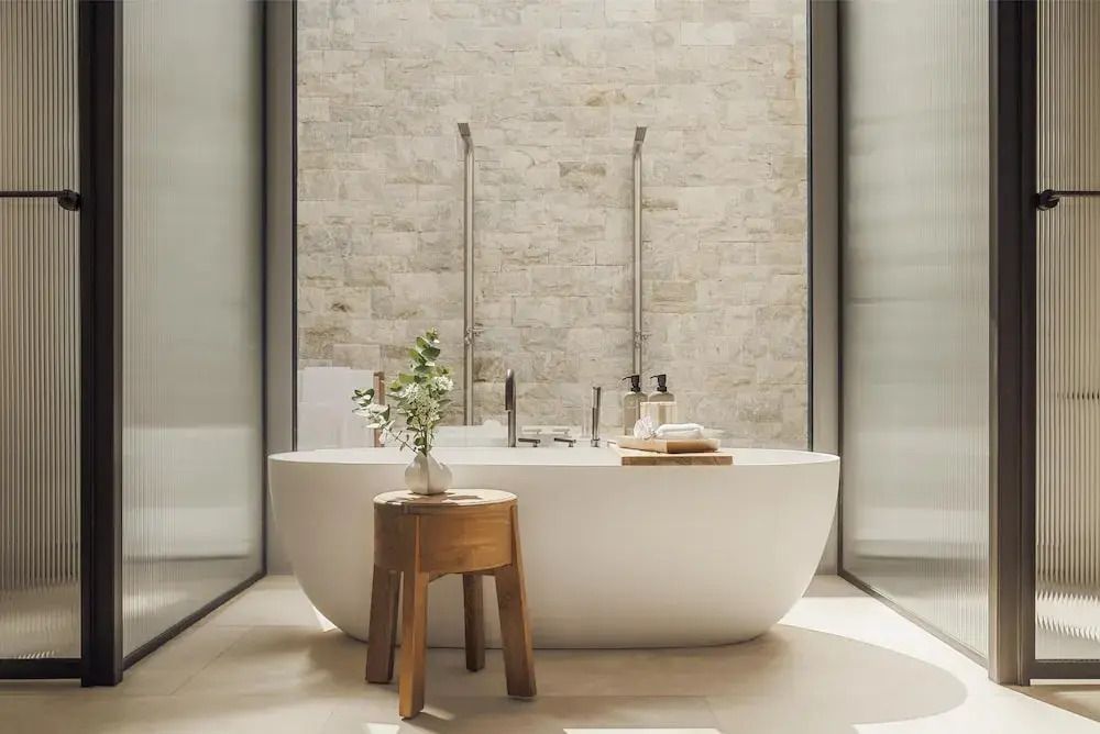 Luxuriöse freistehende Badewanne vor Steinwand mit natürlichem Licht