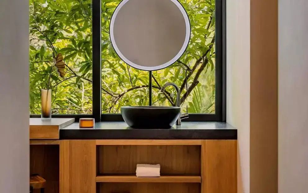 Modernes Badezimmer mit rundem Spiegel und Blick ins Grüne