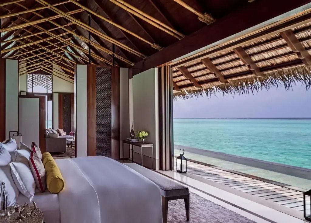 Luxus-Schlafzimmer in Wasser-Villa mit Blick über türkisfarbenes Meer und Himmel.