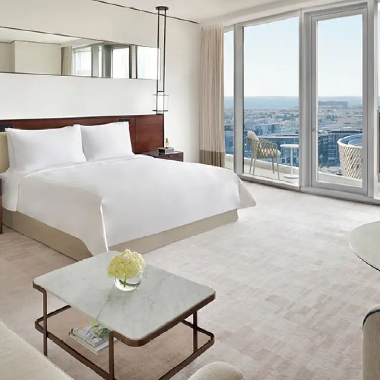 Helles Schlafzimmer mit Doppelbett und Stadtblick aus großen Fenstern.