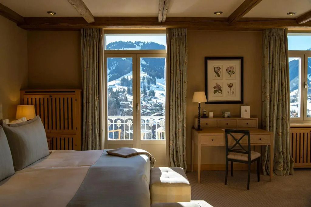 Gemütliches Doppelzimmer mit Blick auf verschneite Berge durch große Fenster.