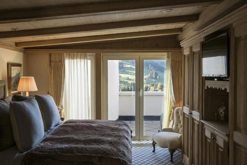 Elegantes Schlafzimmer mit Holzbalken und Blick auf die Berge durch große Fenster.